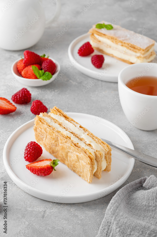 Traditional French dessert millefeuille with vanilla cream and fresh berries on a white plate on a gray concrete background.
