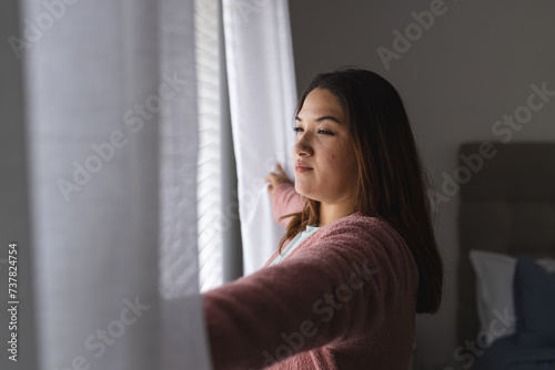 Young plus size Biracial woman looks out the window thoughtfully at home photo