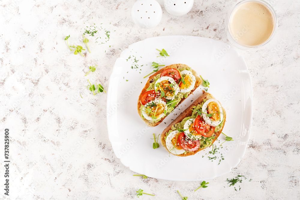Delicious toast with avocado, boiled egg, tomatoes and microgreen on a white plate. Healthy eating, breakfast. Keto diet food. Trendy food. Top view