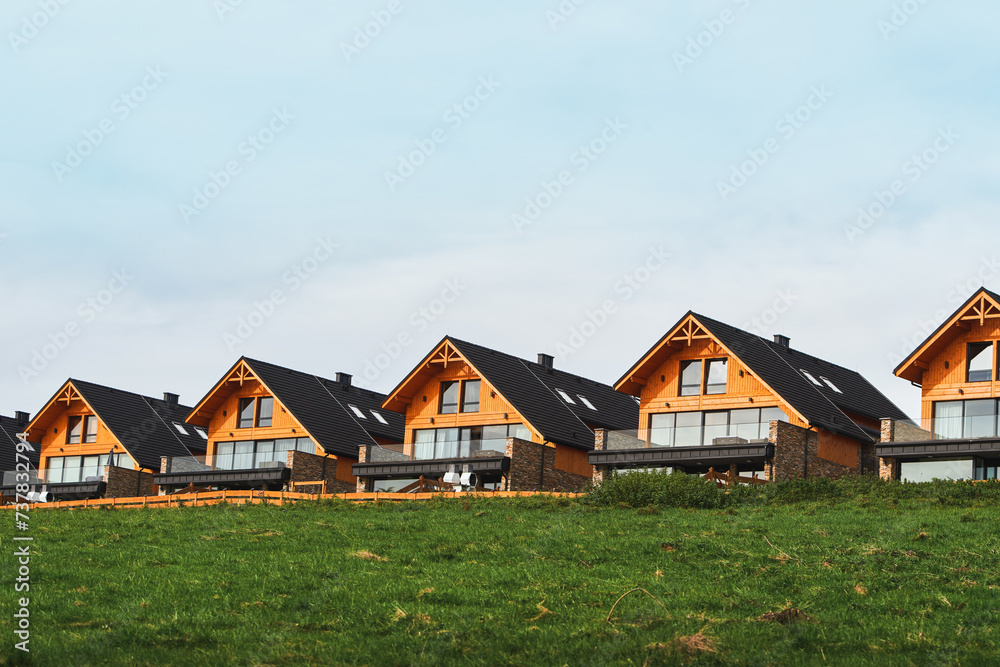 Wooden houses with modern design and architecture on a grassy hill overlooking the fields and the sky. Wooden houses with modern design and architecture on a grassy hill overlooking the fields and the sky.