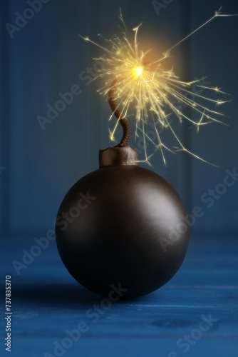 Old fashioned black bomb with lit fuse on blue wooden table