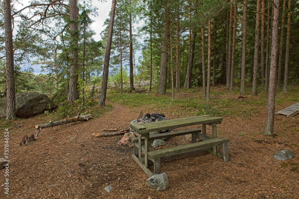 Camping fire behind table and benches on the island of Linlo in forest, Kirkkonummi, Finland.