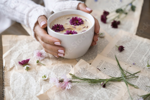 Female hands holding a cup of cappuccino with flowers on a book background
