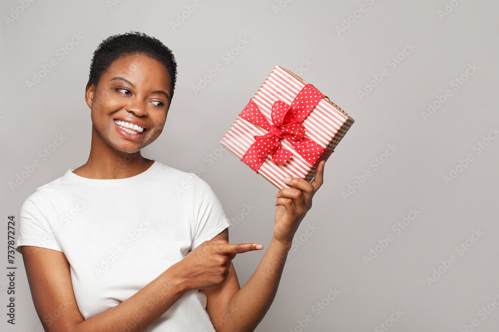 Young healthy woman holding colorful gift present box and pointing finger on white background. Celebration and holiday concept Young healthy woman holding colorful gift present box and pointing finger on white background. Celebration and holiday concept