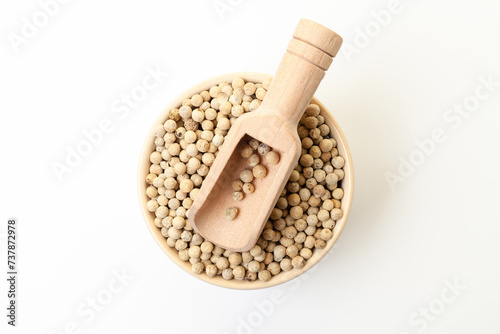 White peppercorns in bowl with wooden scoop on white background. Dry white pepper grain