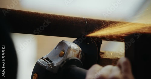 Cutting old metal tube with angle grinder. Over the shoulder shot of skillful construction worker. photo