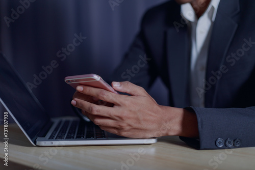 Businessman's hands holding mobile phone and using laptop computer to work from home business success concept..