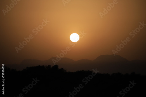 setting sun above a mountain range in hazy sahara desert dust light