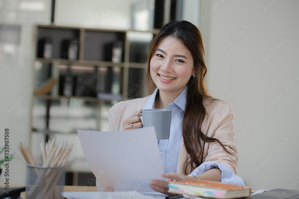 Happy asian young businesswoman using laptop with business finance chart sitting at office working space, Business finance and accounting woman concept. Happy asian young businesswoman using laptop with business finance chart sitting at office working space, Business finance and accounting woman concept.