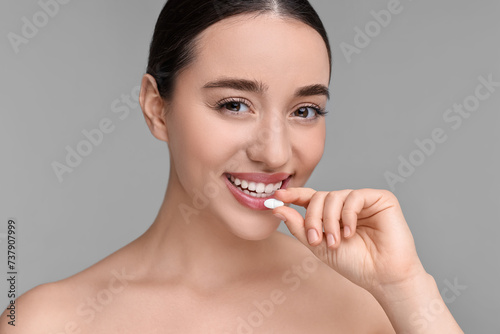 Beautiful young woman with vitamin pill on grey background