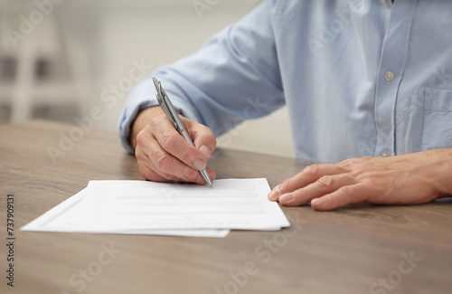 Senior man signing Last Will and Testament at wooden table, closeup photo