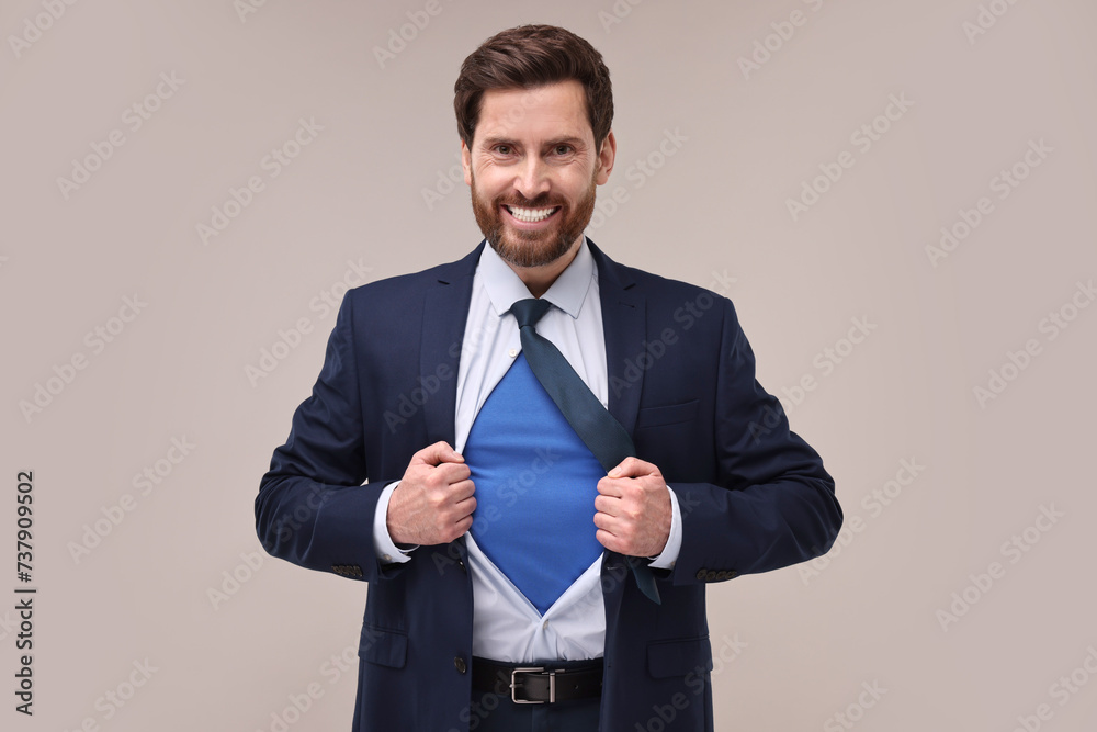 Happy businessman wearing superhero costume under suit on beige background Happy businessman wearing superhero costume under suit on beige background