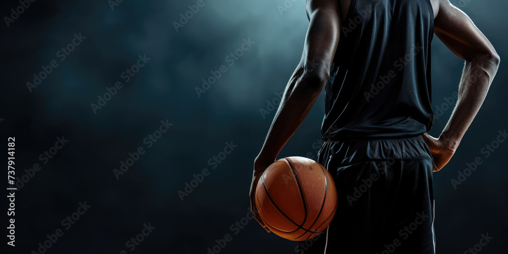 A focused athlete in a dark jersey holds a basketball against a dark background, emphasizing the readiness and determination for the game.	
