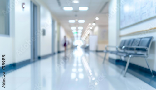 Hospital hall for outpatient with patients, white bright tone, blurred background. A blurred image of a bright and clean hospital corridor with seating.