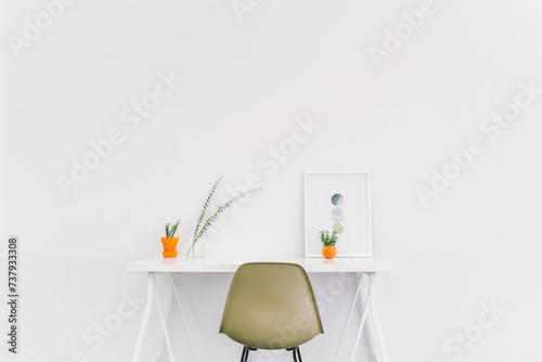 This minimalistic yet cozy interior design of an empty desk with a chair, a picture frame, and a poster on the wall. Minimal home interior design idea.
