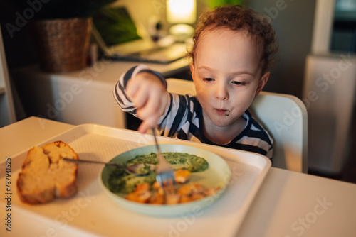A toddler is sitting at the table at home and eating his lunch.