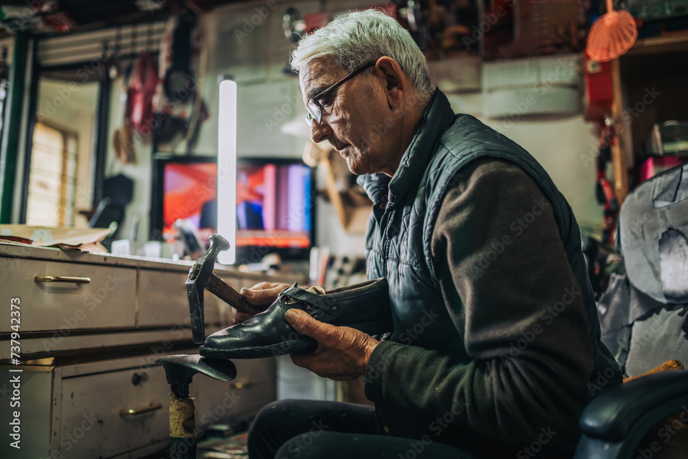 Side view of a senior craftsman repairing footwear at workshop. Side view of a senior craftsman repairing footwear at workshop.