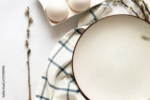 Easter table setting with empty white ceramic plate with cutlery  and spring willow branches on white table. Neutral colors.