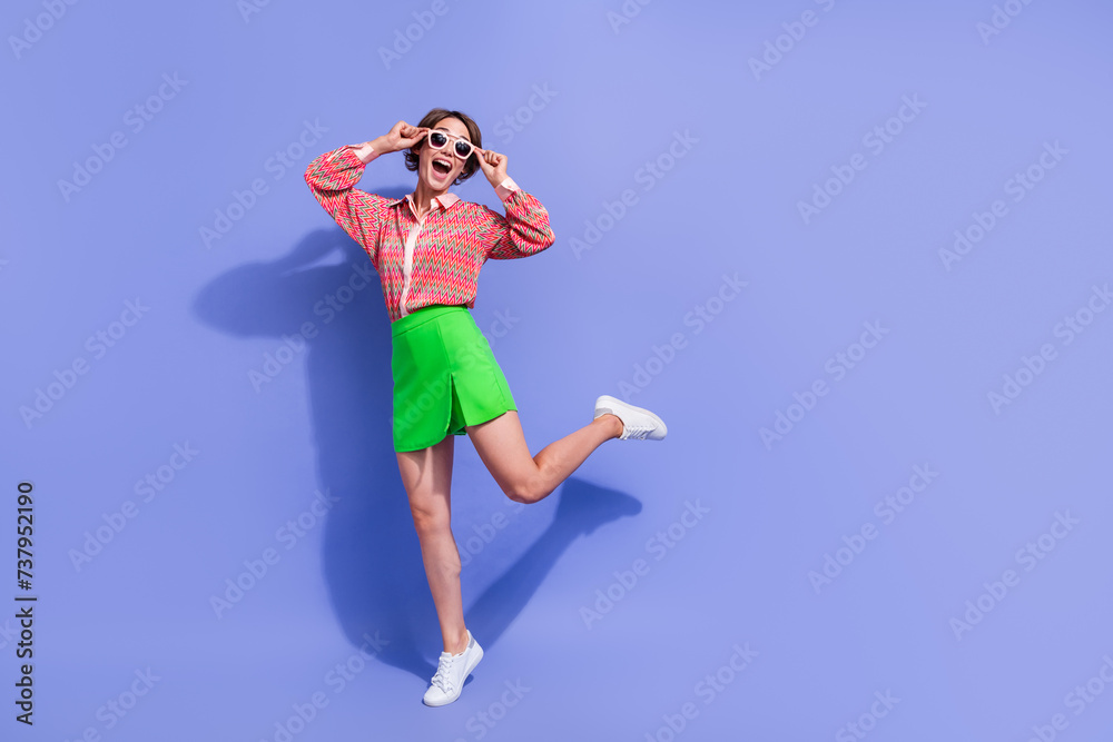 Full length photo of impressed girl touching sunglass wear green skirt staring at unbelievable sale isolated on blue color background Full length photo of impressed girl touching sunglass wear green skirt staring at unbelievable sale isolated on blue color background