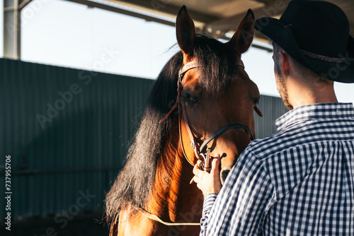 Man taking care of his brown horse in an equestrian center © PEDROMERINO