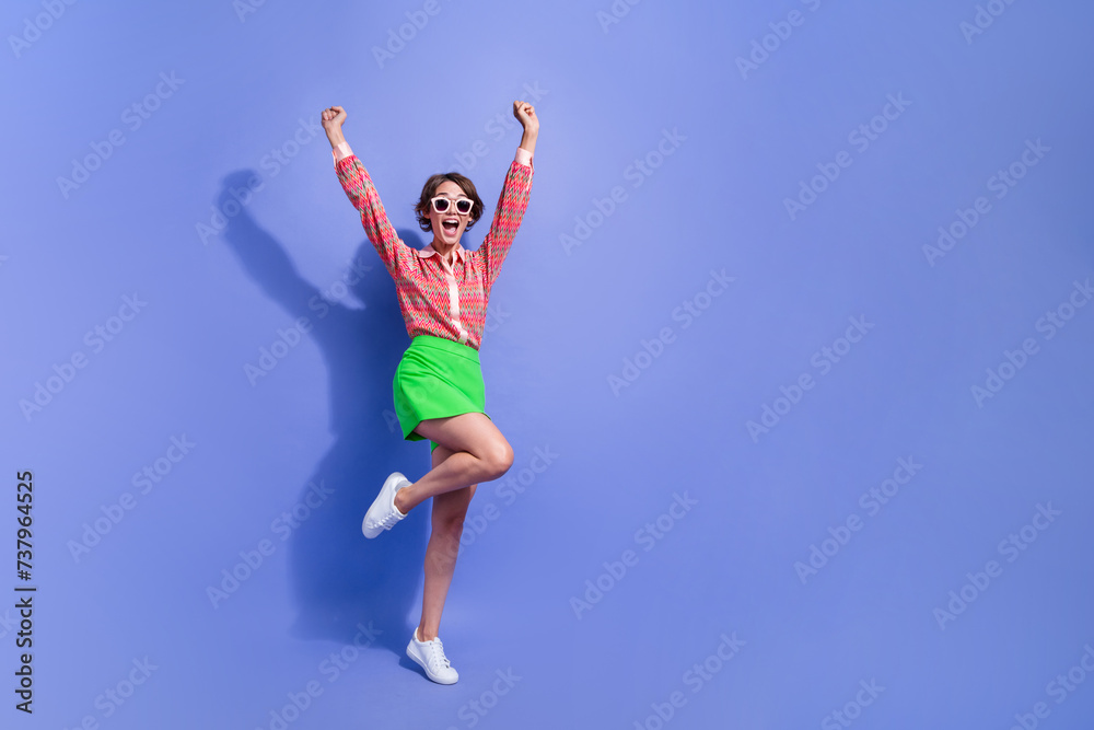Full size photo of overjoyed woman dressed print shirt in sunglass raising up fists win lottery scream isolated on blue color background Full size photo of overjoyed woman dressed print shirt in sunglass raising up fists win lottery scream isolated on blue color background