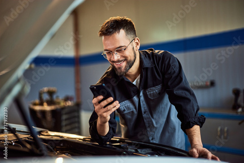 A smiling mechanic receives a message on his phone while working at his car service. photo