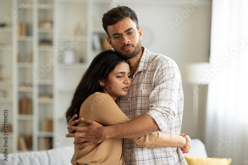 Loving indian man hugging, comforting and supporting his wife feeling sad and depressed, unhappy couple having relationship trouble