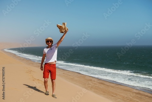 Holding jacket in hand. Tourist is walking on the sand near the sea