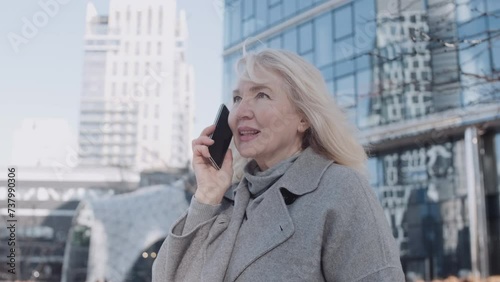 A senior woman talking by phone holding tulips outdoors