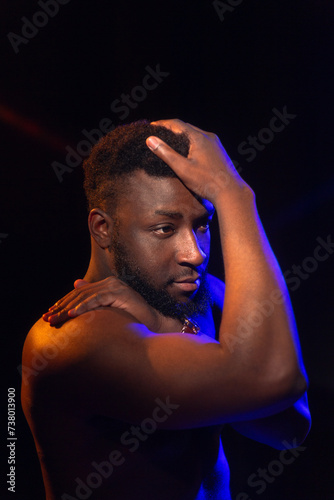 Studio portrait of a young man with a naked torso with blue-red backlighting on a black background. © Eno1