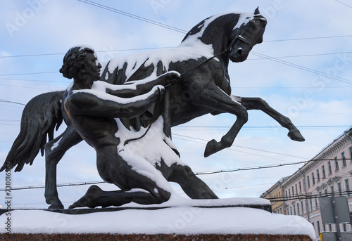 Saint Petersburg on snowy winter day. View of the famous Anichkov Bridge with beautiful sculptures by Peter Klodt Taming Horses across  Fontanka River on Nevsky Prospekt on sunny cold day photo
