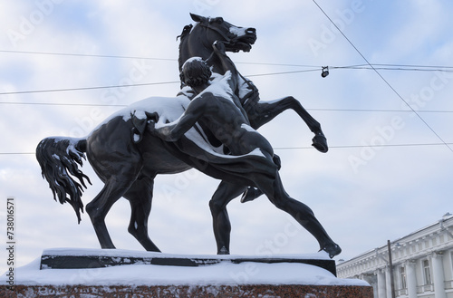St. Petersburg on snowy winter day. View of the famous Anichkov Bridge with beautiful sculptures by Peter Klodt Taming Horses across; Fontanka River on Nevsky Prospekt on sunny cold day photo