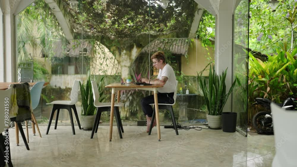 Transgender individual focuses on laptop in modern, airy coworking ...
