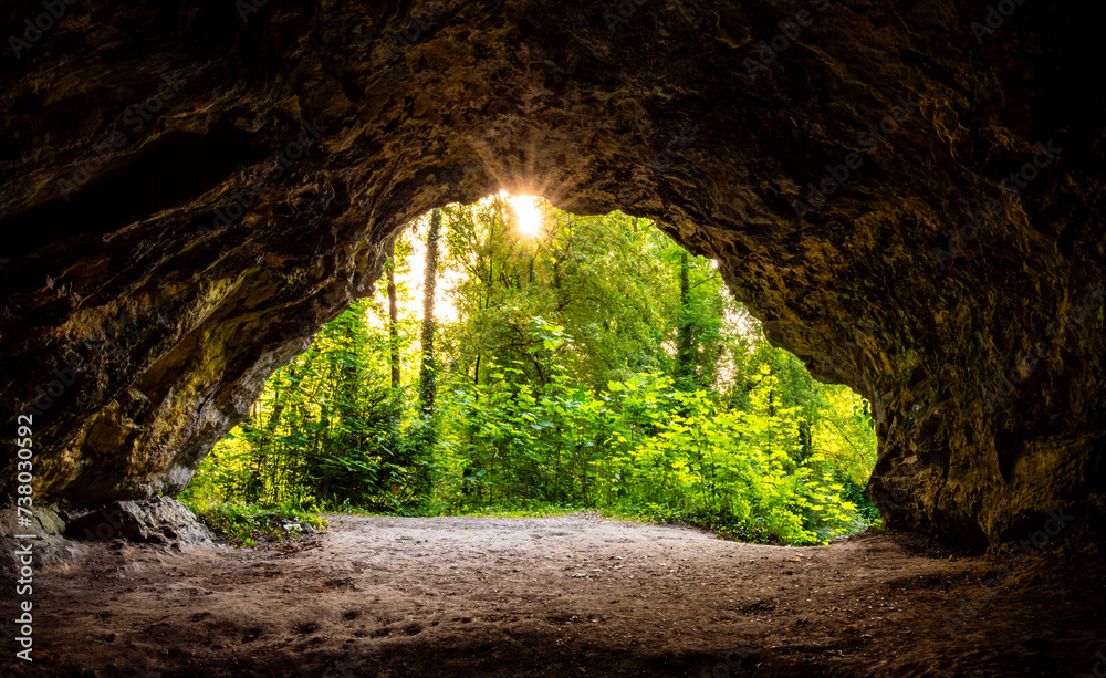 Panoramic view from a small cave (Perick Caves) in a limestone quarry in a nature reserve in Hemer in Sauerland, Germany. Sunlight shines through the lush vegetation inside the cave and illuminates it