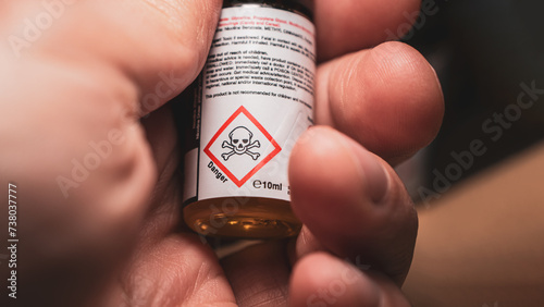 Hand holding a small bottle of e-cigarette nicotine liquid, displaying a danger skull sign, indicating potential health risks associated with vaping.
