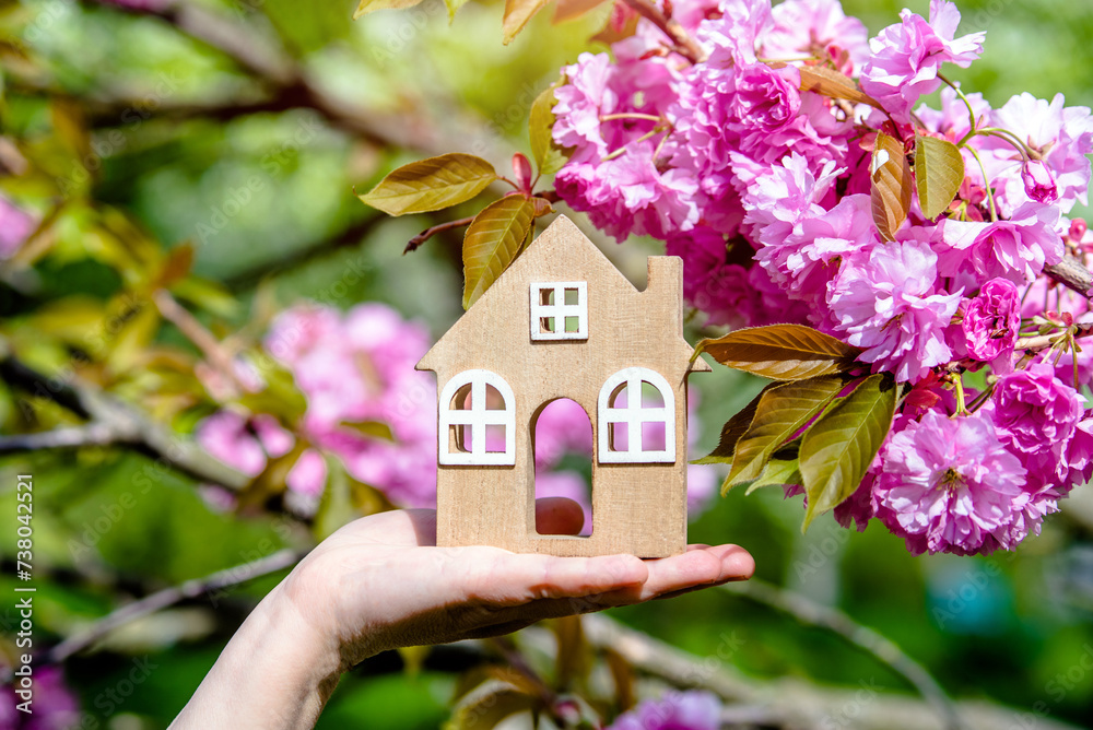 The girl holds the house symbol against the background of blossoming Sakura
