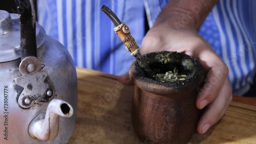 Tradiciones Argentinas de la yerba mate. El hombre coloca el chorrito de agua caliente con la vieja pava o tetera de aluminio en el mate de calabaza sobre la mesa de madera, formando un original video photo