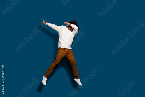 Full length photo of excited good mood guy dressed white pullover jumping high having fun empty space isolated dark blue color background