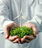 Man holding a wind turbine with green grass in his hands