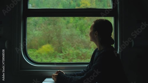 Young woman staring at mountains through train window. Girl traveling by train enjoying nature landscape view from transportation, traveling by train concept