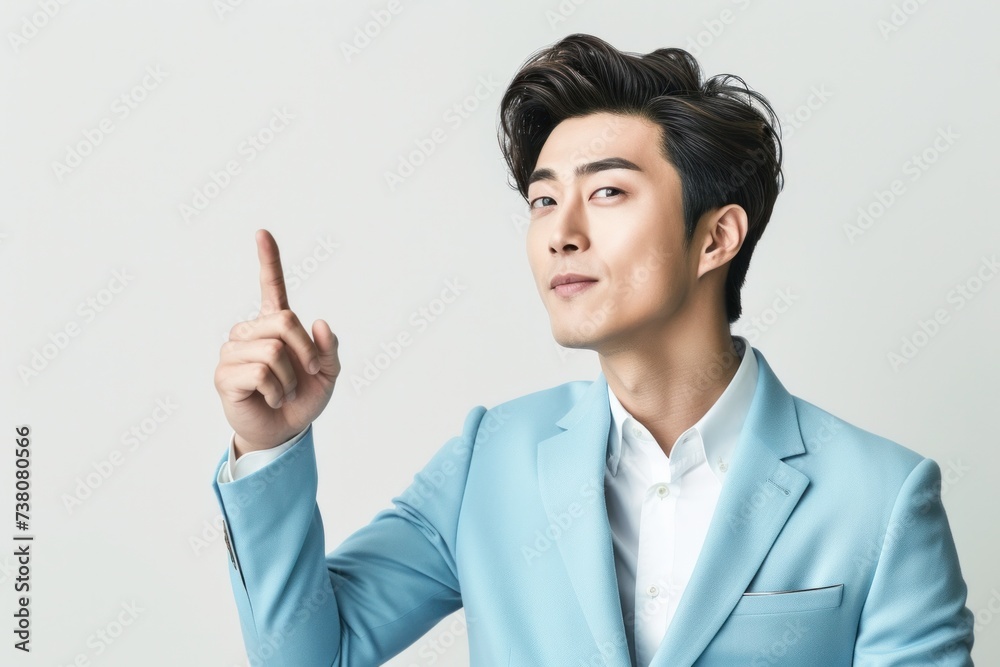 Young handsome Korean businessman wearing a light blue suit on a white background, isolated, pointing his finger sideways. with copy space Young handsome Korean businessman wearing a light blue suit on a white background, isolated, pointing his finger sideways. with copy space