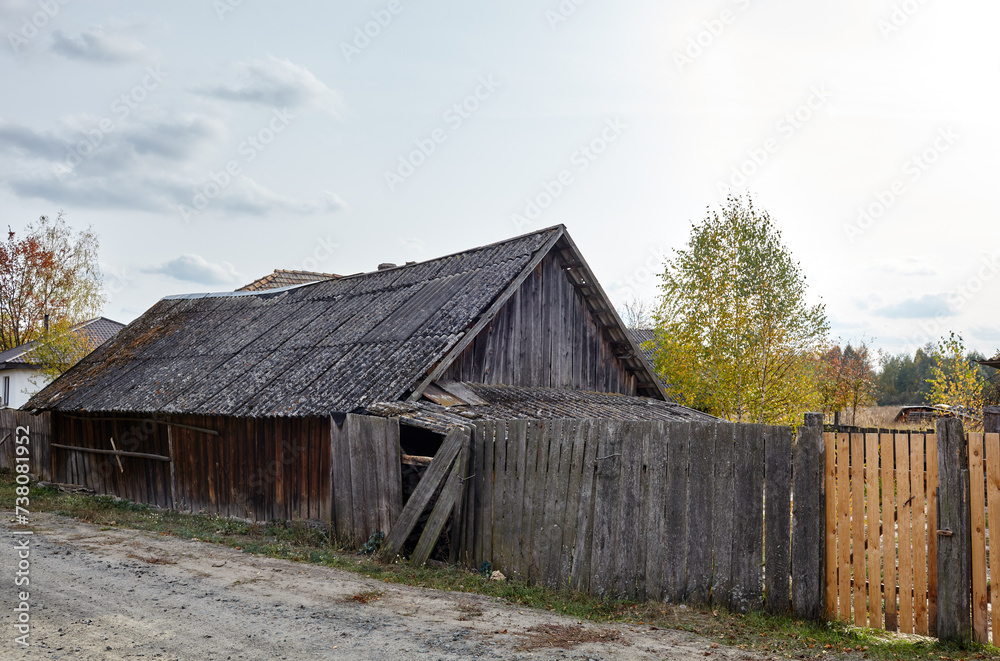 Obraz premium Old barn with wooden fence in countryside. Road in the village, summer rural landscape