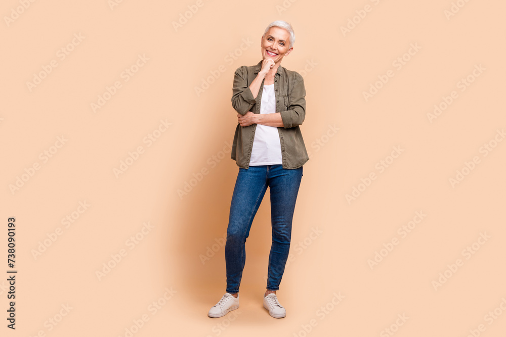 Full size photo of pretty senior female touch chin thoughtful dressed stylish khaki outfit isolated on beige color background Full size photo of pretty senior female touch chin thoughtful dressed stylish khaki outfit isolated on beige color background