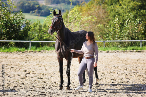 Horse with bridle and glittery browband, standing next to the owner in the riding arena.