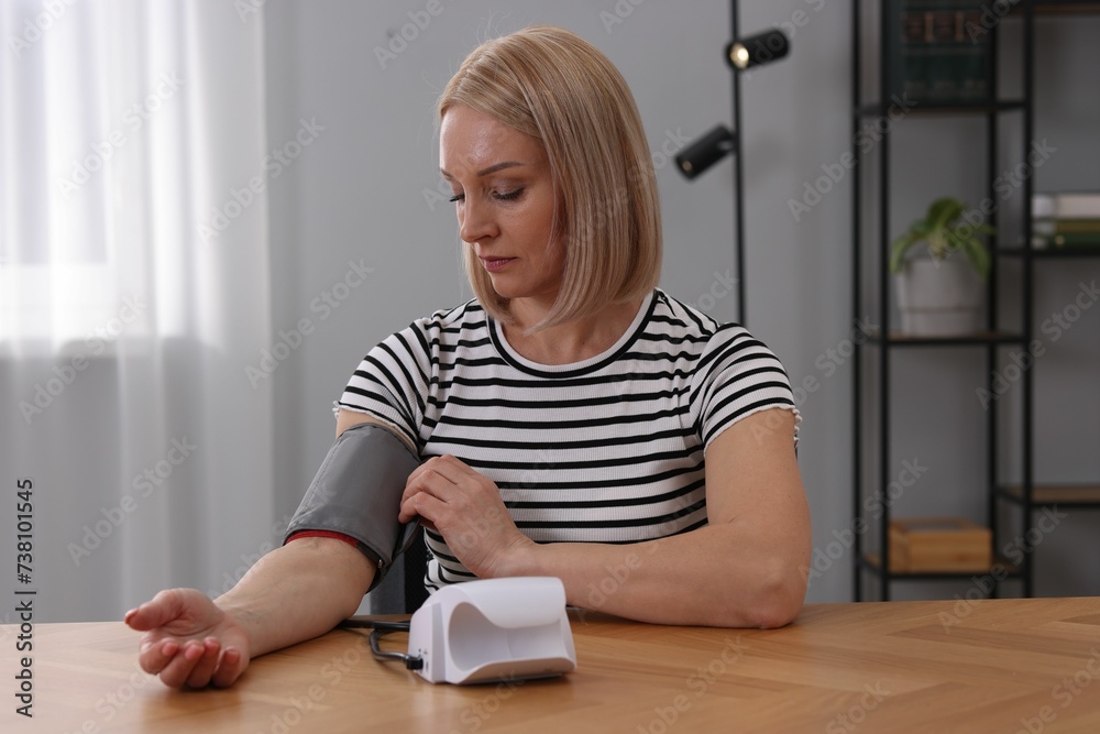 Woman measuring her blood pressure with tonometer at wooden table indoors Woman measuring her blood pressure with tonometer at wooden table indoors