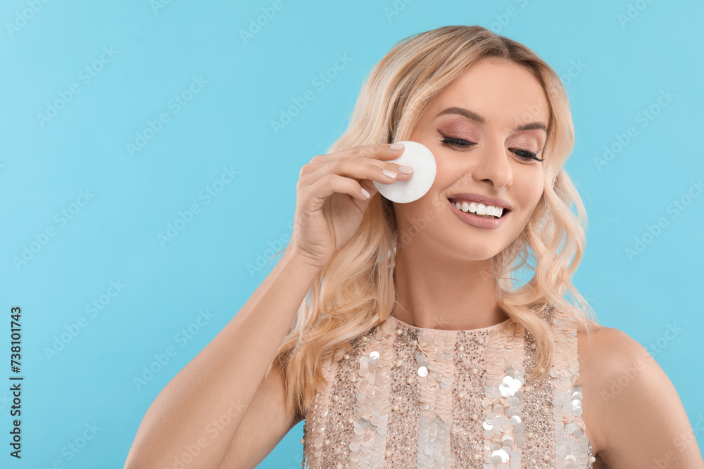 Smiling woman removing makeup with cotton pad on light blue background. Space for text Smiling woman removing makeup with cotton pad on light blue background. Space for text