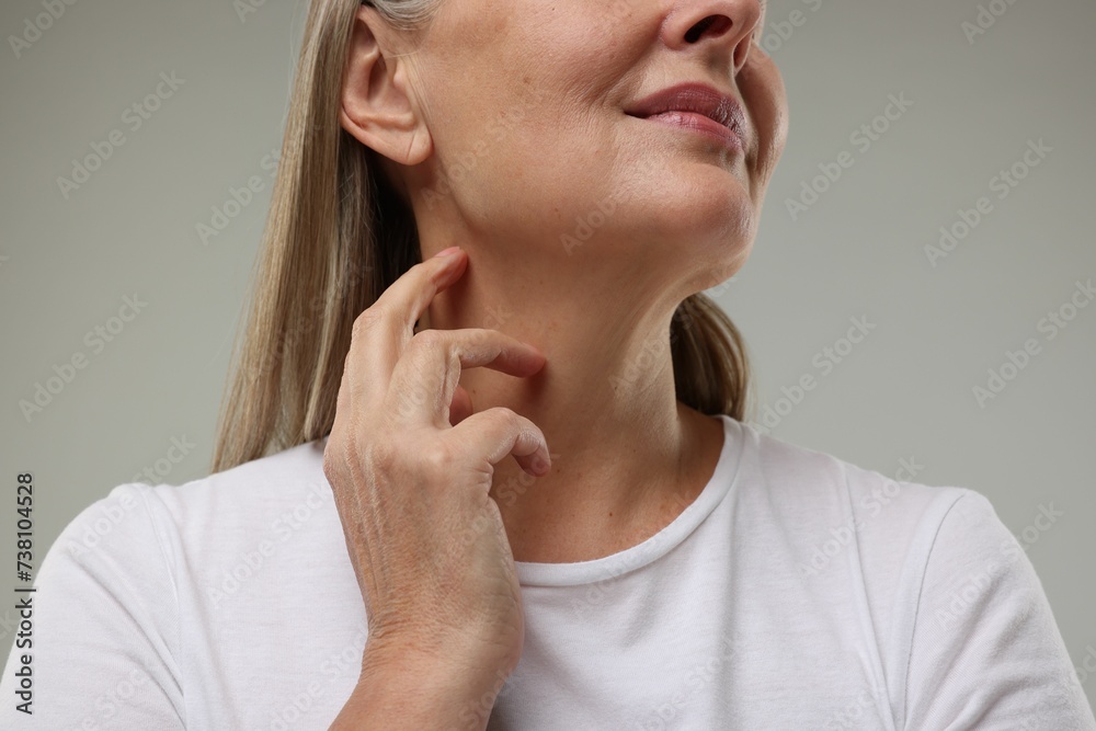 Mature woman touching her neck on grey background, low angle view Mature woman touching her neck on grey background, low angle view
