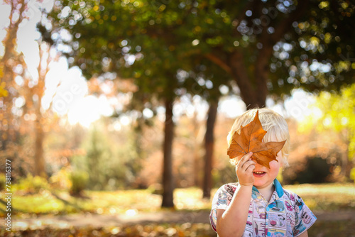 Toddler boy playing in fallen Autumn leaves with large leaf hiding face photo