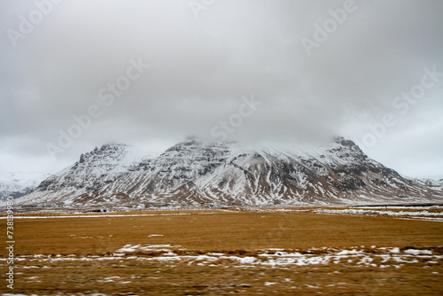 Snow-capped mountain viewed from a moving car on an overcast day. Tourism in Iceland in Winter