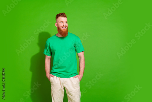 Portrait of good mood cool guy with long red beard wear stylish t-shirt look at promo empty space isolated on green color background